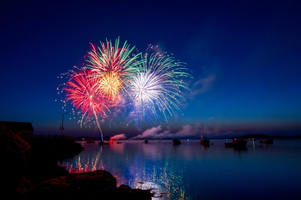 Colourful fireworks illuminate a navy blue sky over a large body of water.